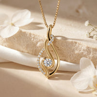Yellow gold moissanite swirl pendant with round solitaire on a styled stone background.