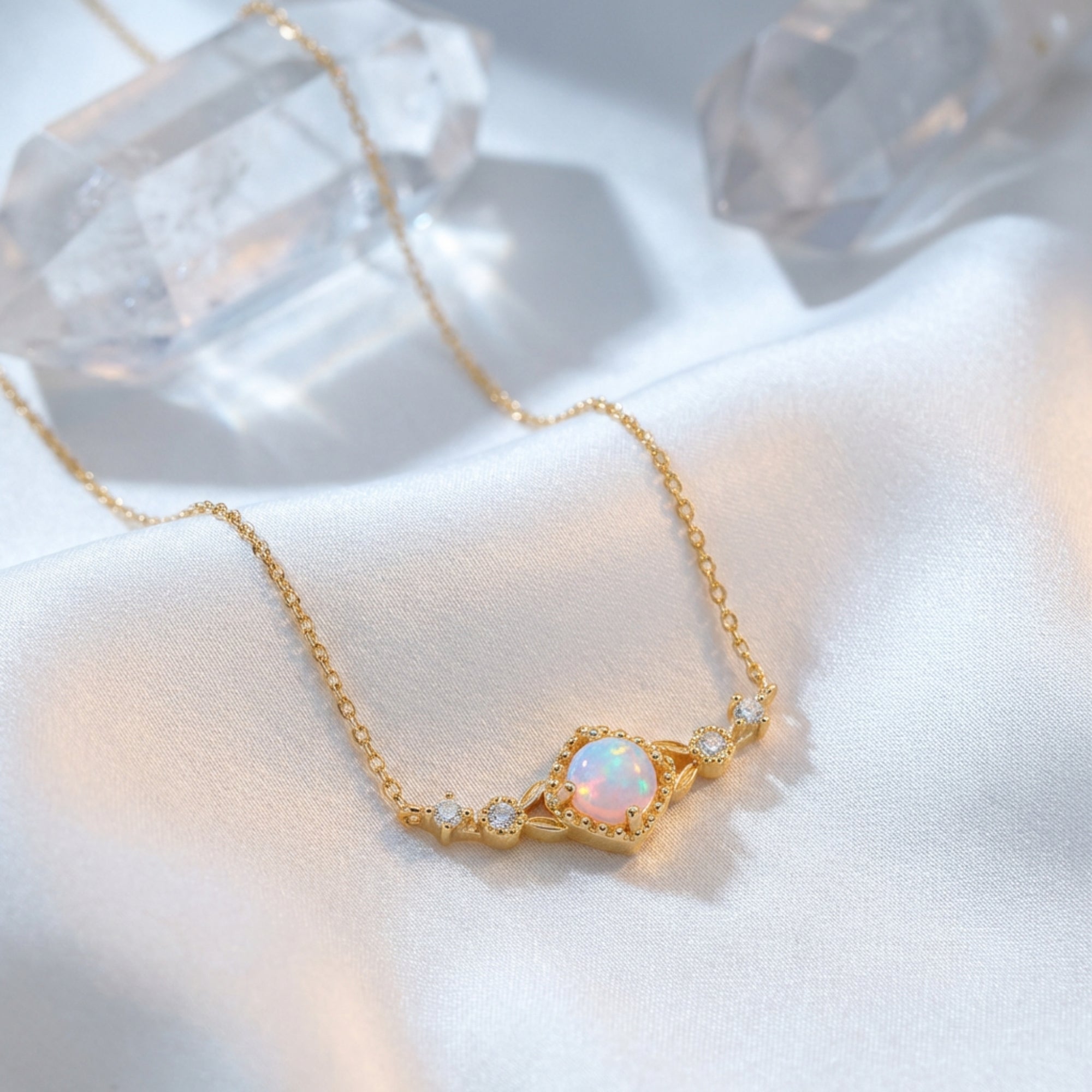 Gold-tone sterling silver necklace with a round white opal pendant displayed on white silk with quartz crystals.