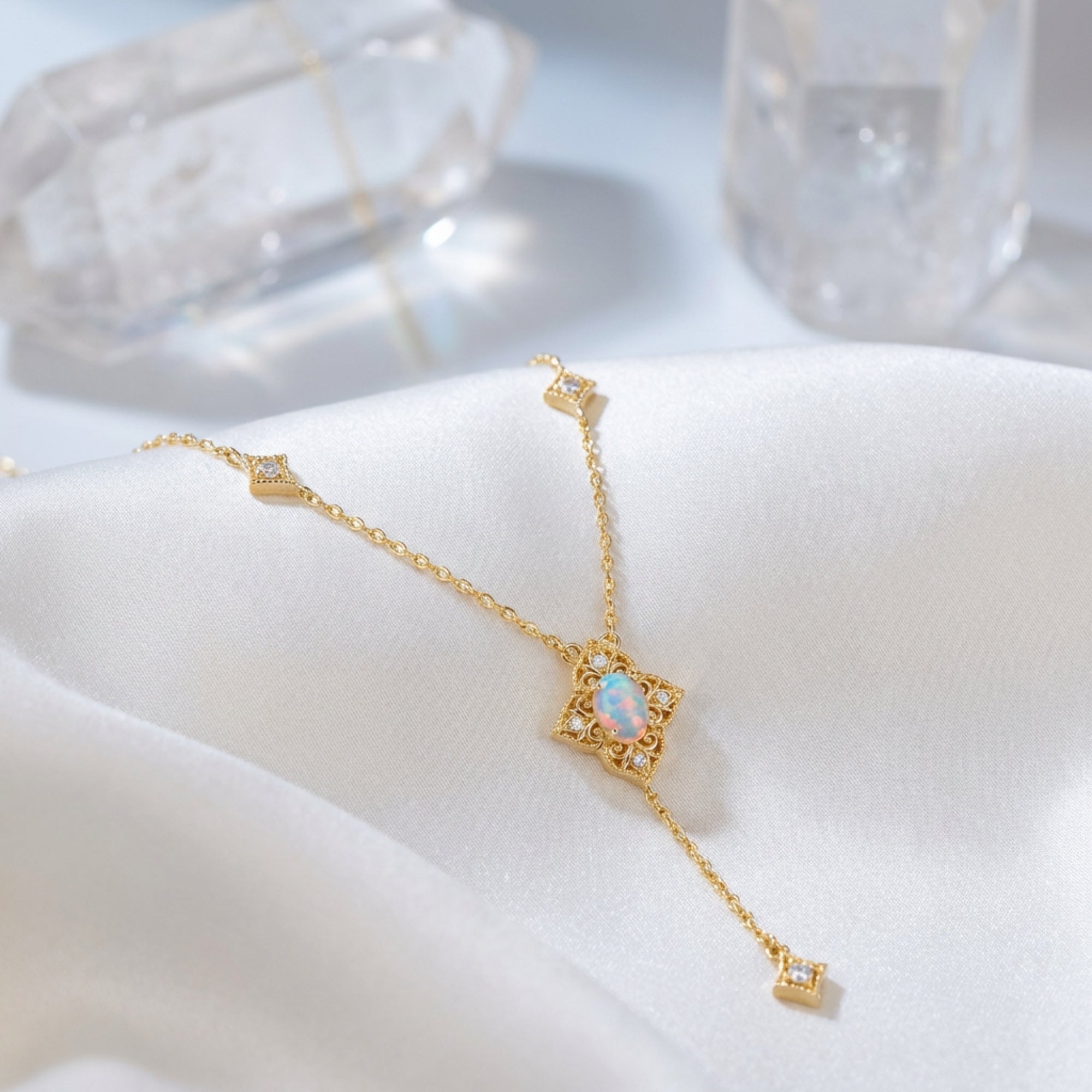 Gold-tone lariat necklace with an oval white opal pendant displayed on white silk fabric with crystals.