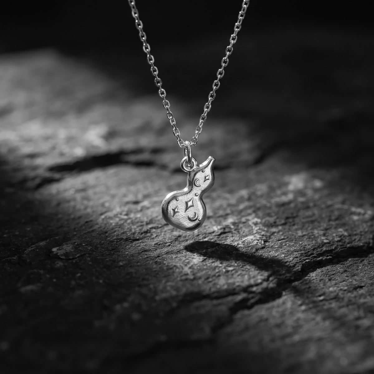 Silver gourd pendant with engraved stars and crescent moon, suspended above dark slate.