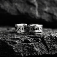 Front view of a textured silver ring with “This too shall pass” stamped on the band, set on dark stone.