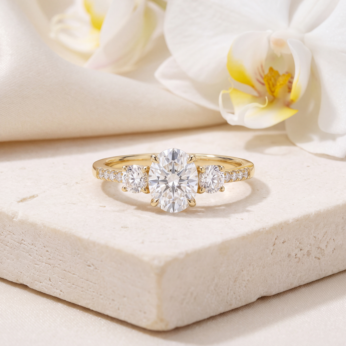 Front view of a three-stone oval moissanite ring in yellow gold with pavé accents resting on a stone block.