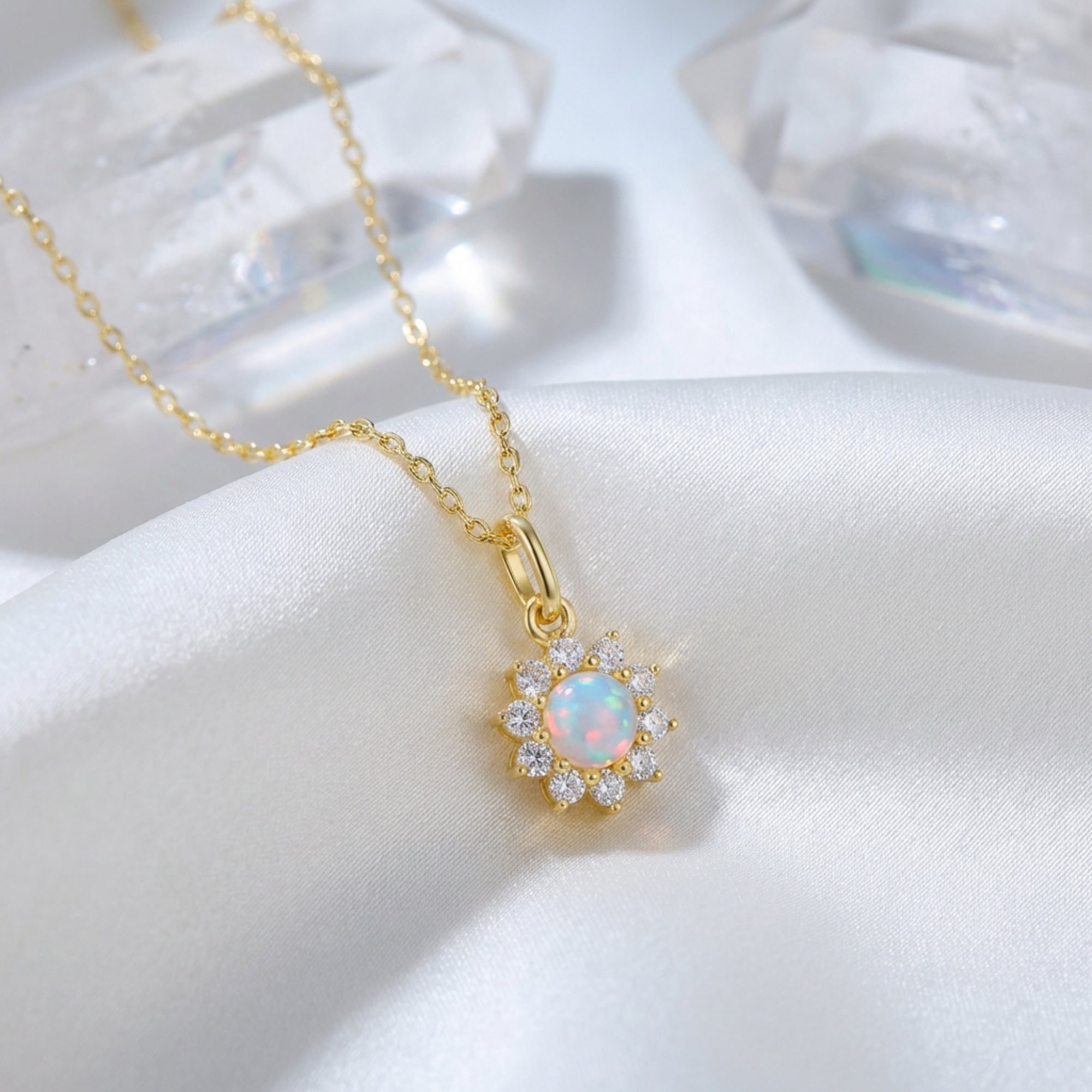 Gold-tone Celestria round white opal pendant necklace with a halo of clear stones on white silk fabric.