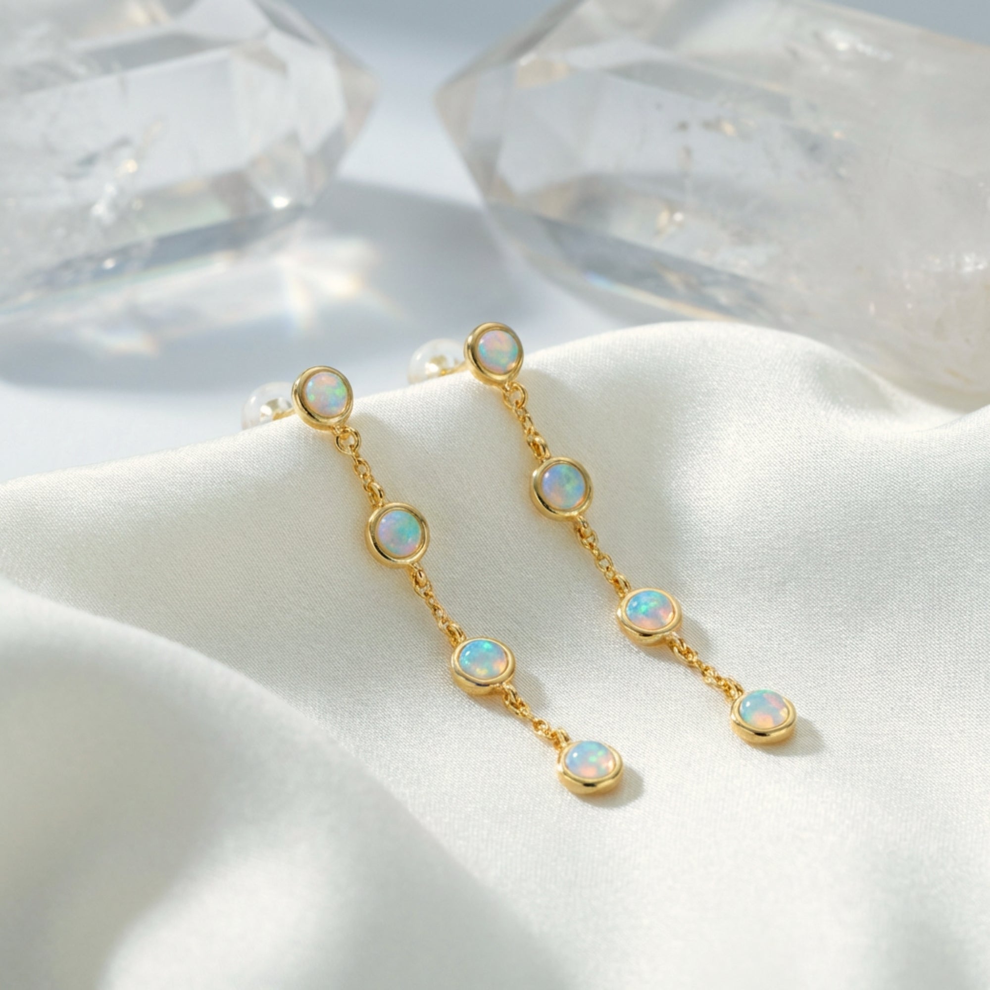 Gold drop earrings with four round white opals in a linear cascade on white silk with clear crystals.