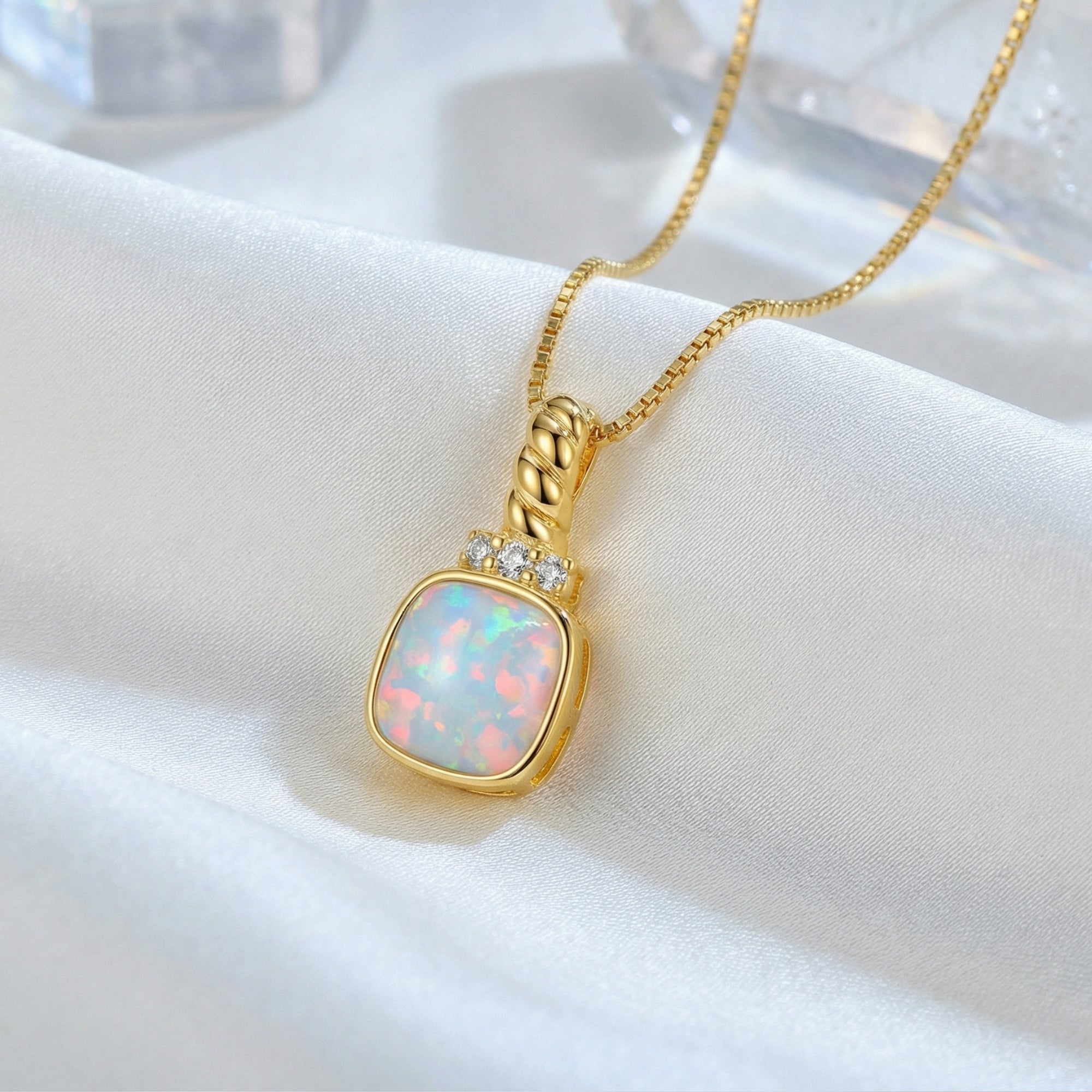 White opal cushion pendant necklace in gold-tone silver resting on white silk fabric.