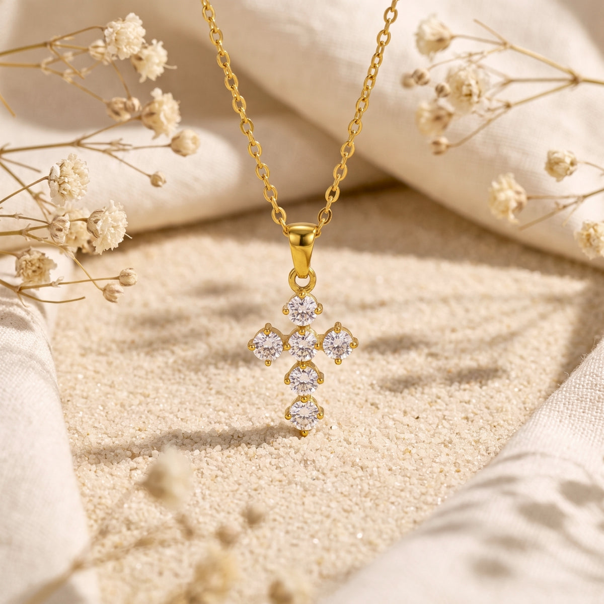 Front view of a gold-tone cross pendant with round clear cubic zirconia stones on fine sand