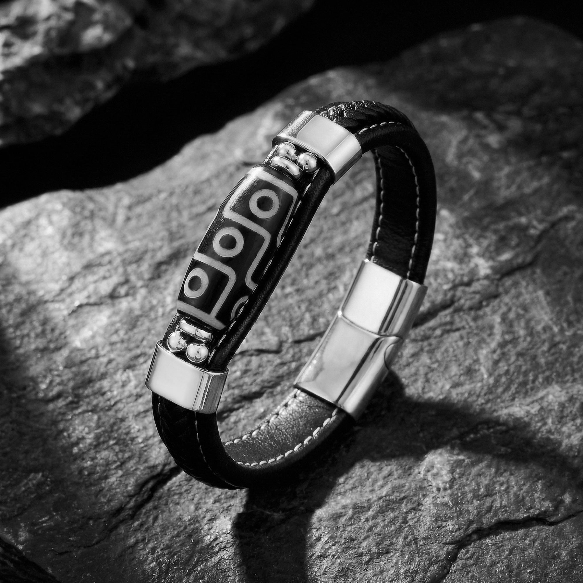 The Echelon men's black braided leather bracelet with silver stainless steel patterned centerpiece on dark rock.