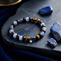 The Stargazer Natural Lapis Lazuli bracelet with round lapis beads and a gold charm on a stone slab.