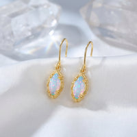 Yellow gold mariquesa-cut white opal drop earrings styled on white silk fabric with decorative crystals.