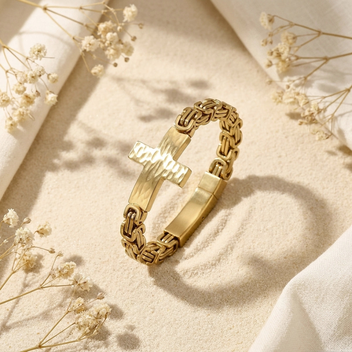 Gold-tone Byzantine chain bracelet with a hammered cross centered on sandy display background.