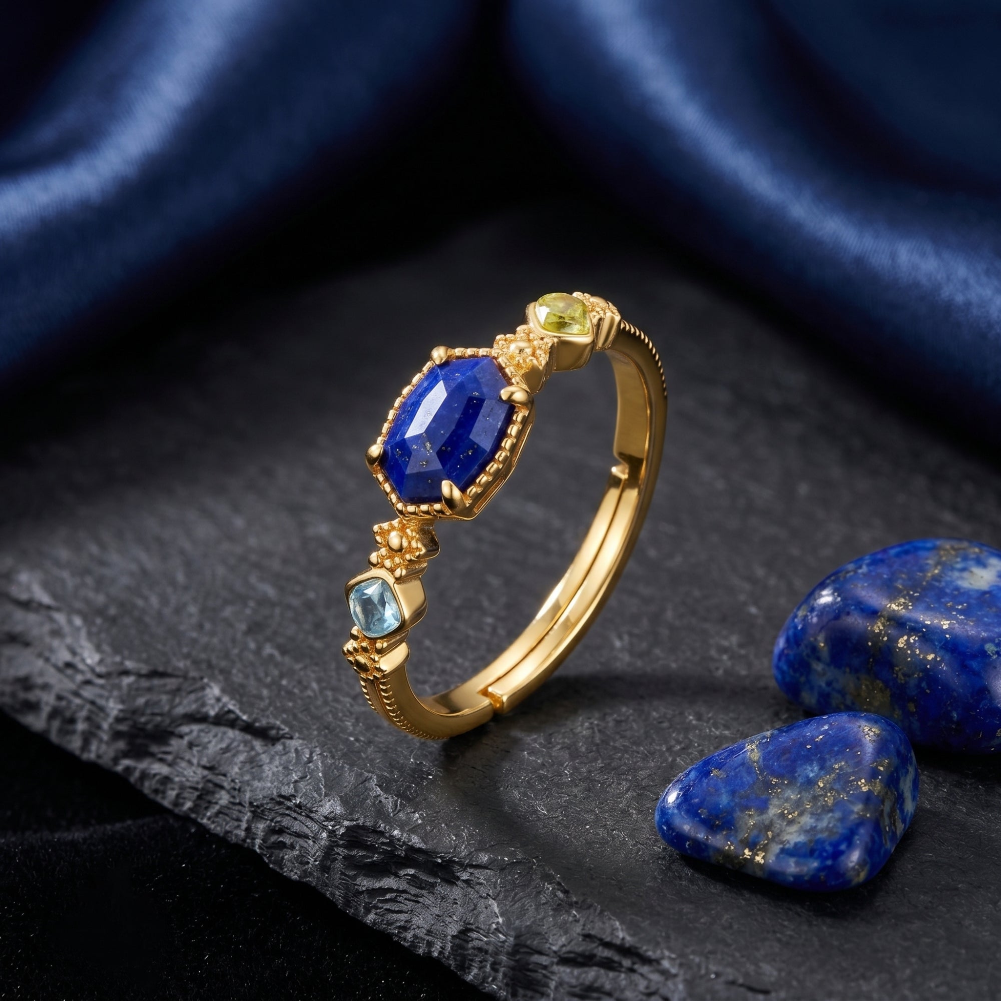 Gold irregular cut lapis lazuli ring with accent stones on a dark slate surface with blue silk.