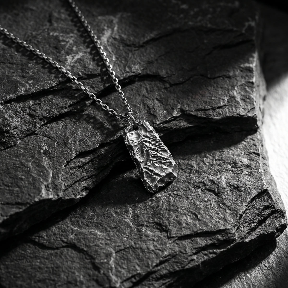 Textured silver ridge pendant necklace resting diagonally on a dark slate surface.