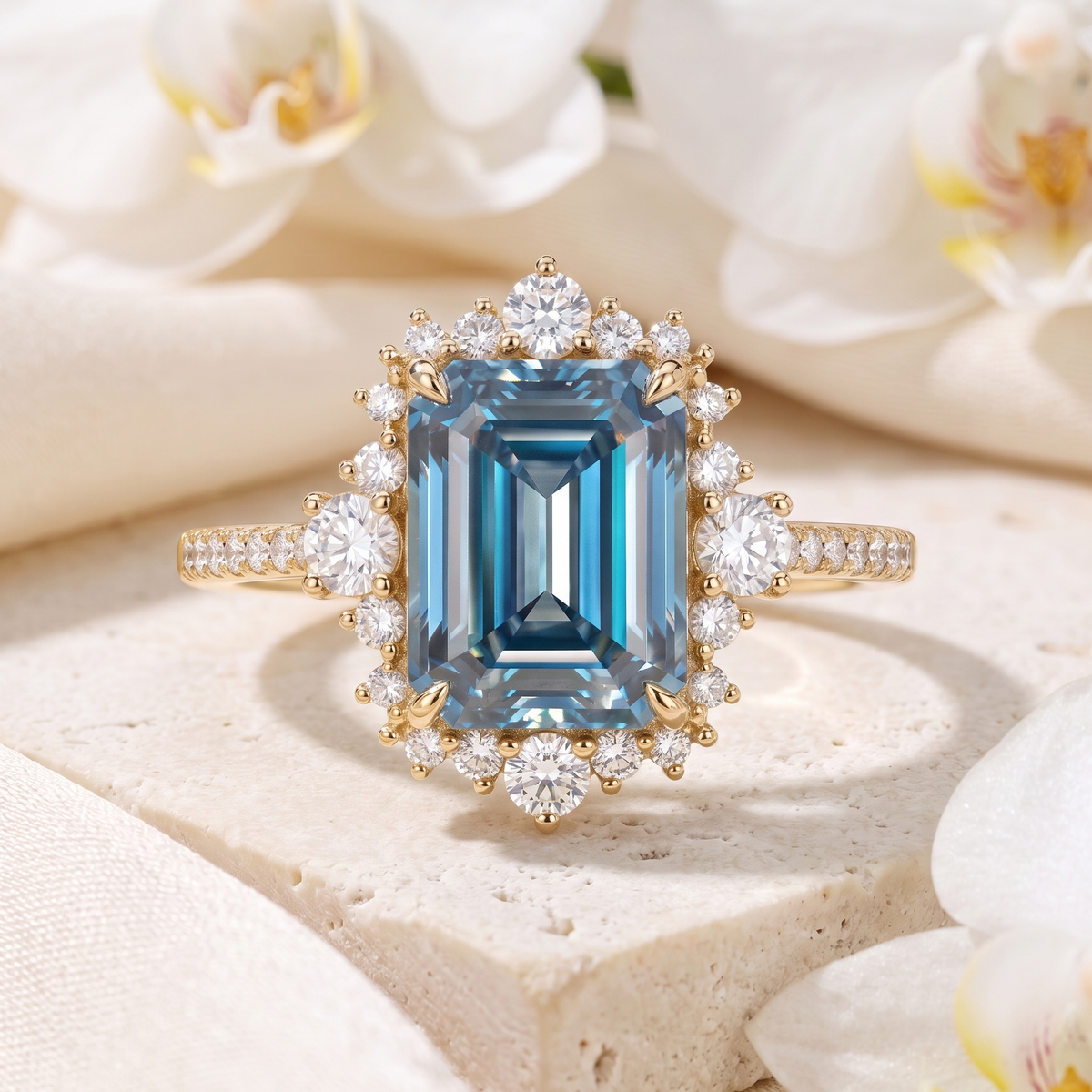 Yellow gold emerald-cut blue moissanite halo engagement ring displayed on a marble surface.
