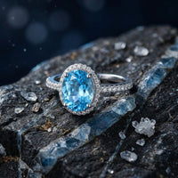 Oval cut natural blue topaz ring in S925 sterling silver halo setting resting on dark textured rock.