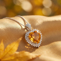 Heart cut citrine necklace in silver with a diamond halo, styled on golden fabric with an autumn leaf.