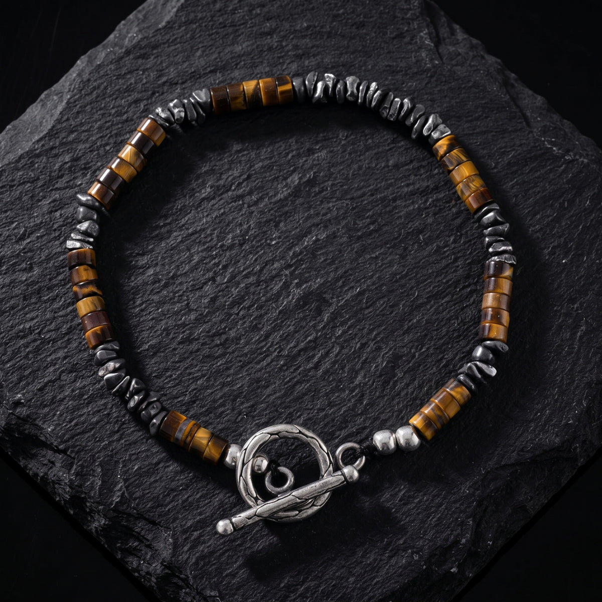 Flat lay of the tiger eye and silver toggle bracelet on a textured dark slate surface.