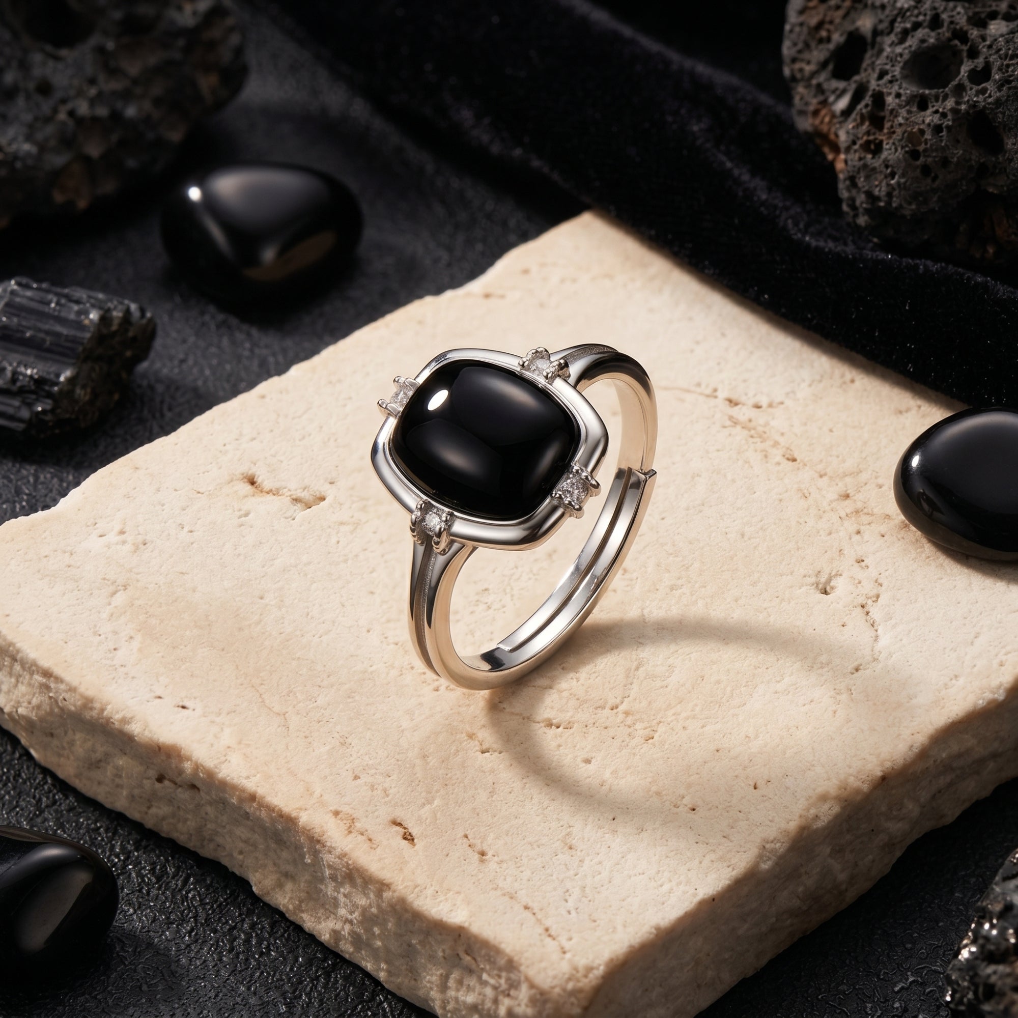 Cushion cut black onyx ring in sterling silver displayed on a stone slab with volcanic rocks in a lifestyle setting.