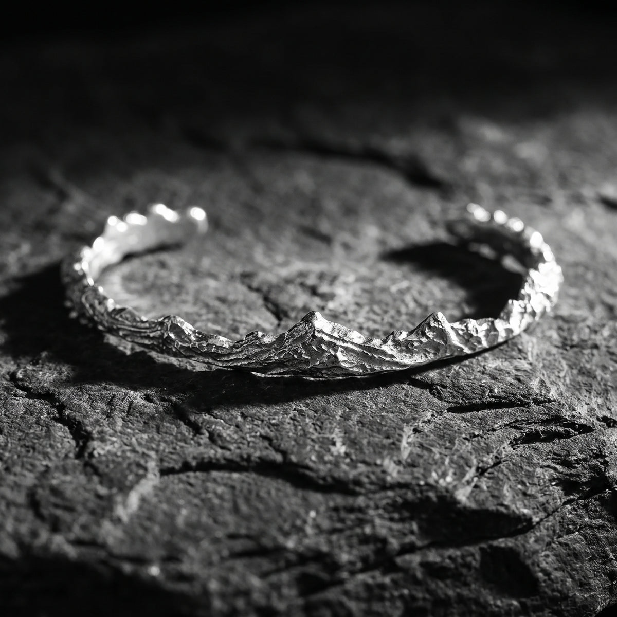 Close-up of a silver mountain ridge open cuff bracelet on dark textured stone.