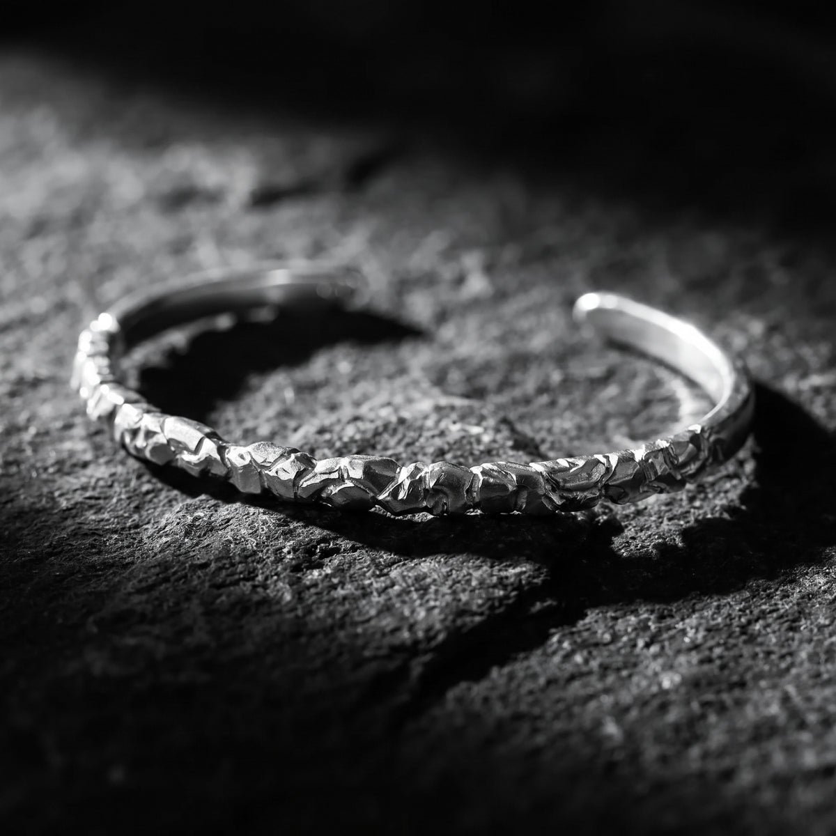 Textured silver carved ridge cuff bracelet resting on dark slate under dramatic lighting.
