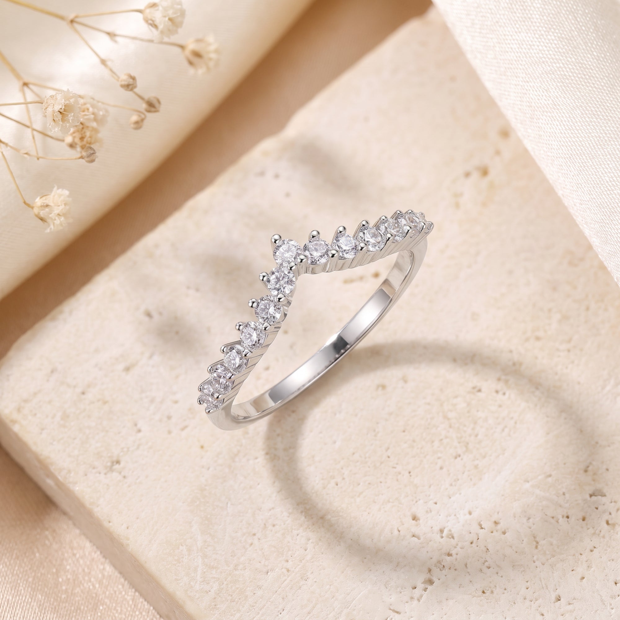 Silver chevron wishbone ring with round cubic zirconia on a stone surface.
