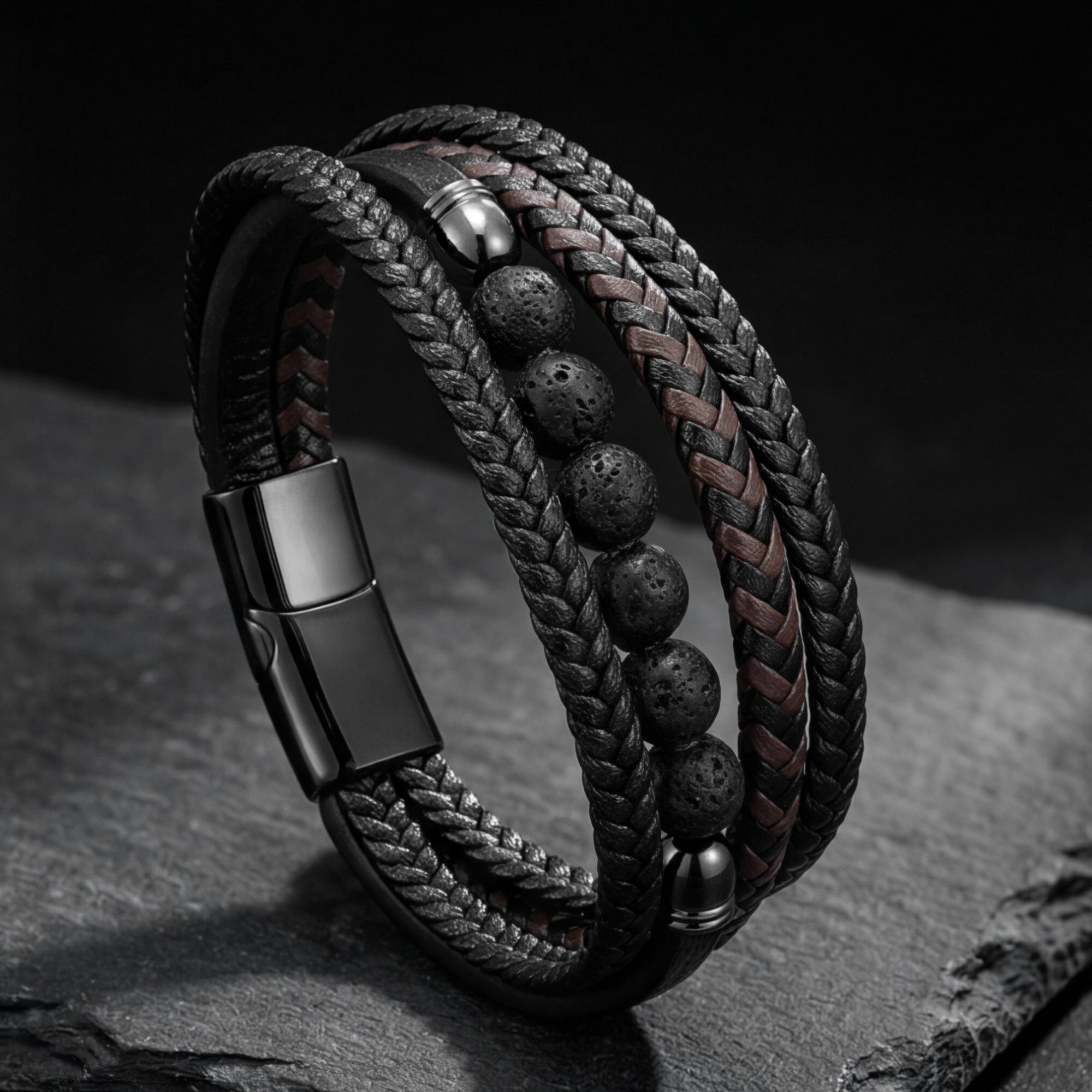 Multi-strand Outrider bracelet with black braided leather, lava stones, and black stainless steel on a stone prop.