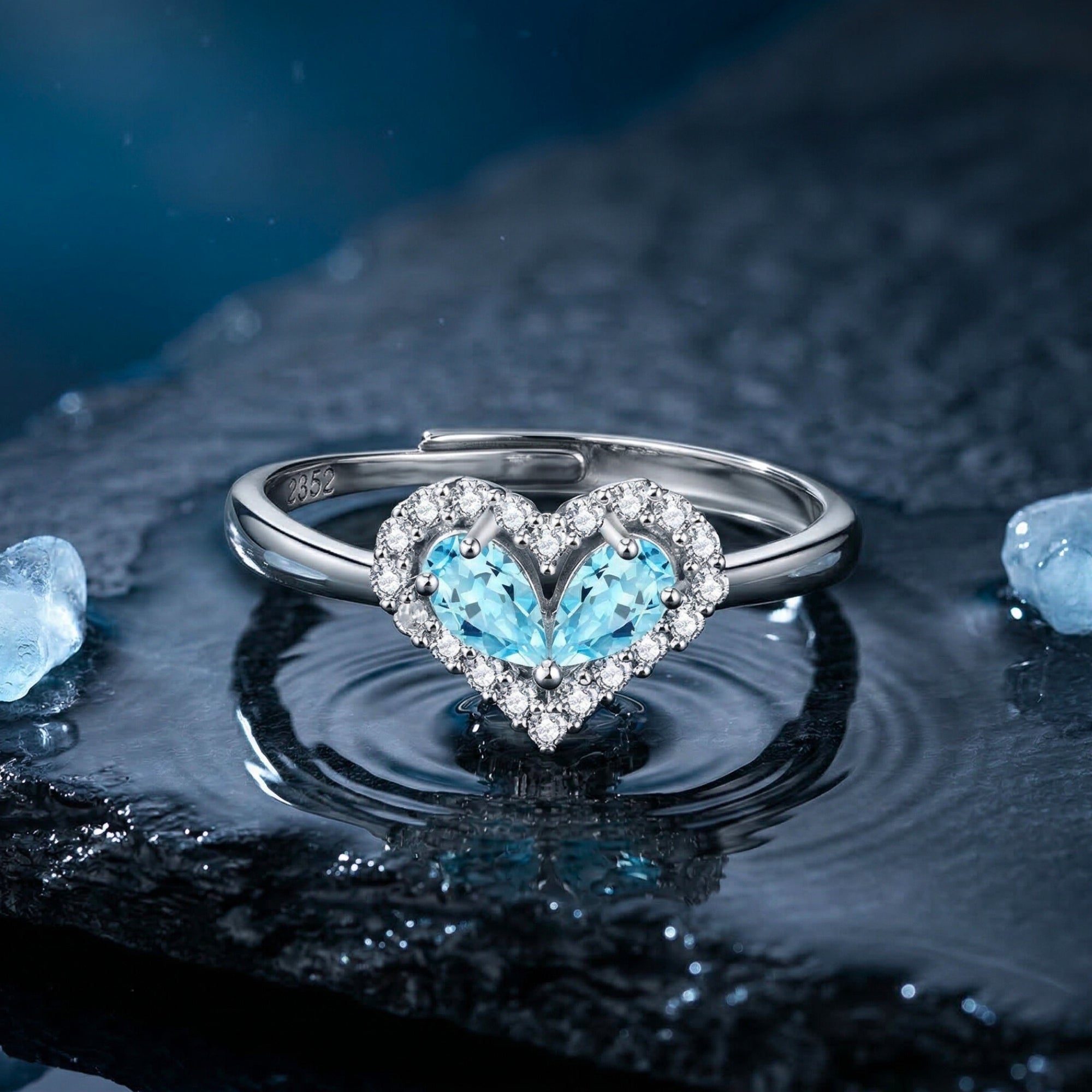 Heart-shaped pear-cut aquamarine halo ring in white gold on a wet stone surface with water ripples.