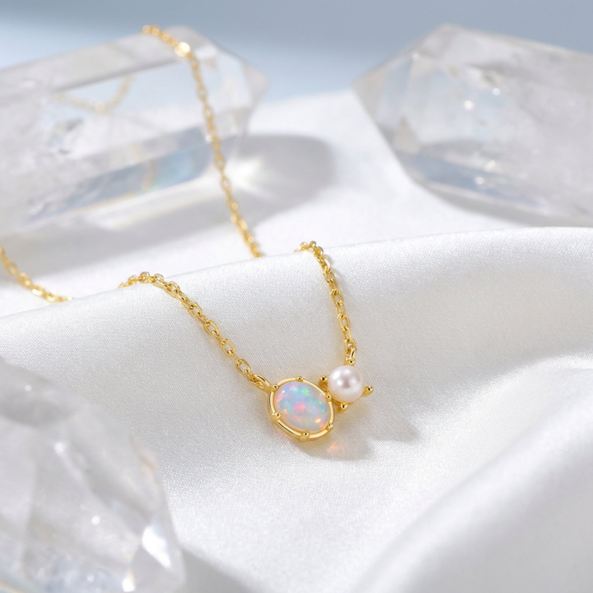 Gold oval white opal and pearl pendant necklace displayed on white silk with quartz crystals.