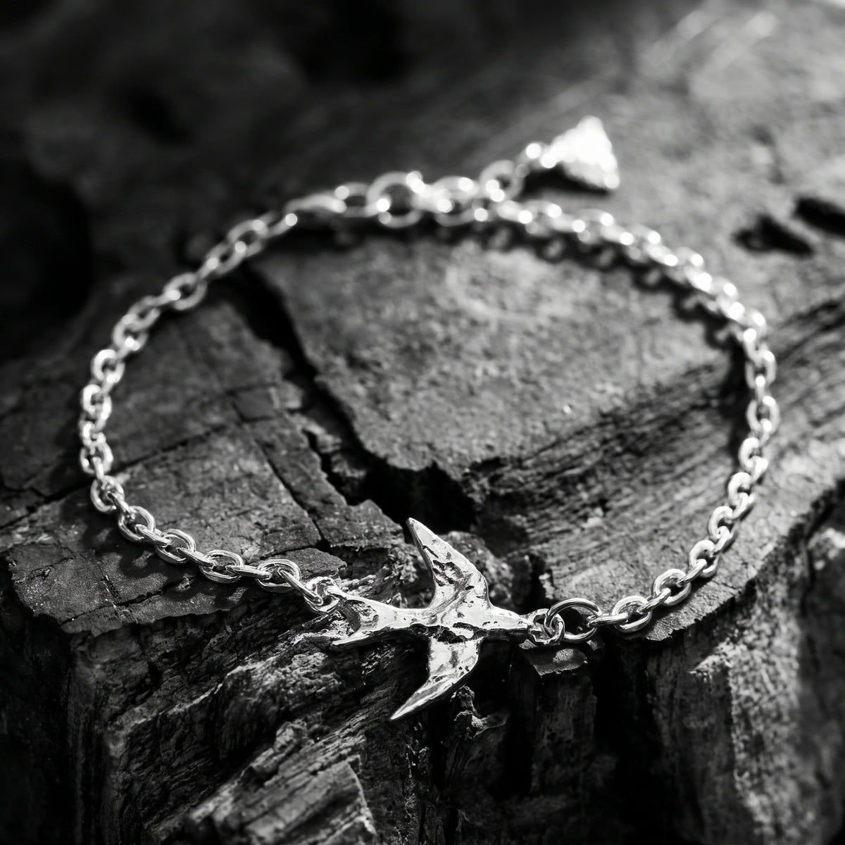 Angled close-up of a silver swallow chain bracelet resting on rough dark wood.