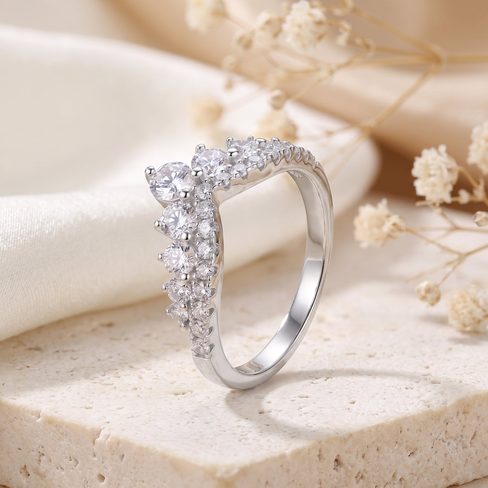 Silver chevron promise ring with round-cut cubic zirconia on a stone surface with dried flowers.