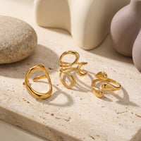 Gold sculptural adjustable ring set on a stone surface with lifestyle props.