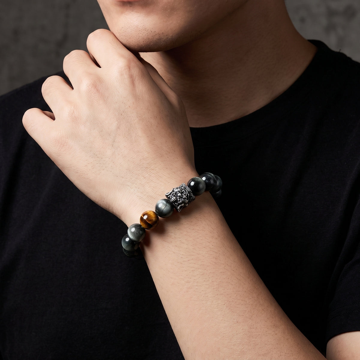 Silver lion bracelet with dark stone beads worn on a person's wrist near their chin.
