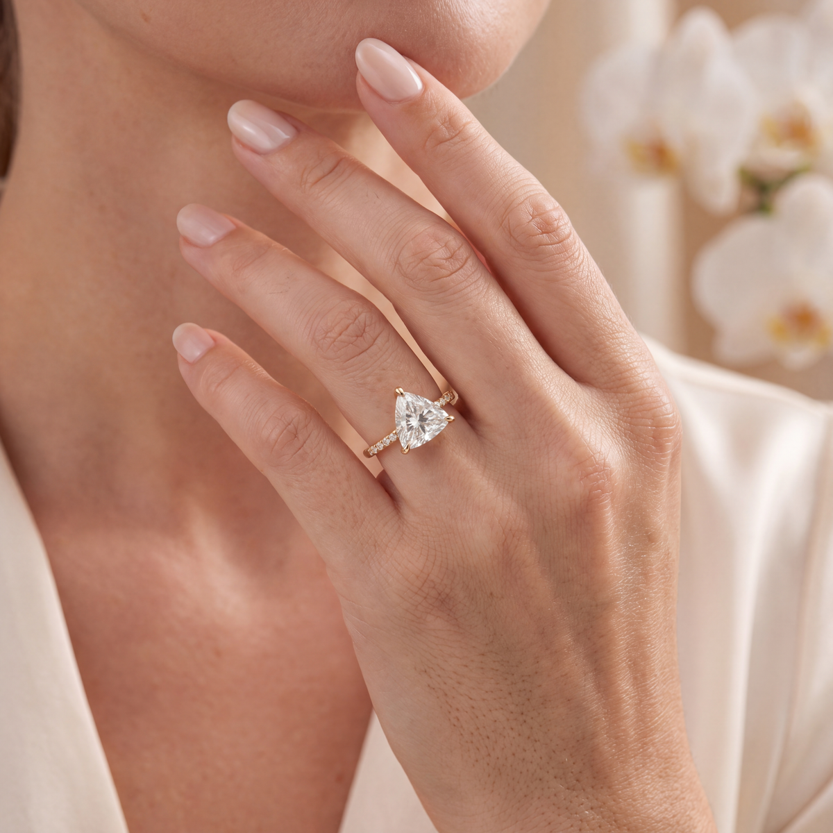 Yellow gold trillion-cut moissanite engagement ring worn on a model's hand touching her chin.