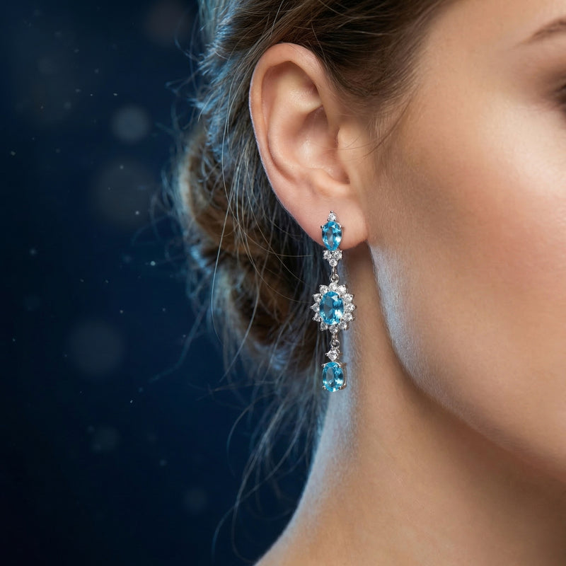 Woman wearing a silver Swiss blue topaz drop earring featuring cascading pear and oval cut gemstones.
