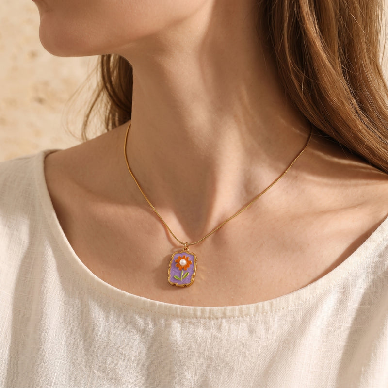 Gold Amorina floral necklace with purple enamel and a pearl center worn by a model on a white linen shirt.