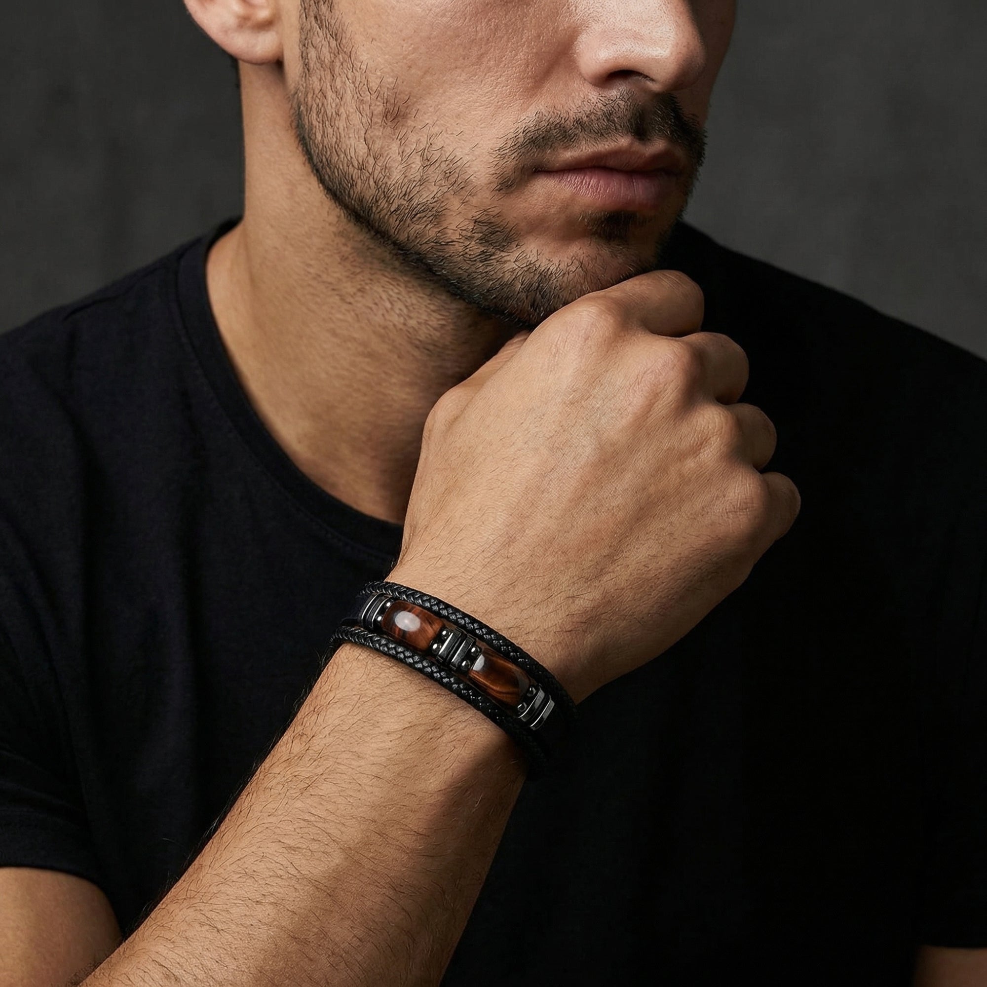 Men's black braided leather bracelet with red-toned accents worn on a wrist by a model in a black shirt.