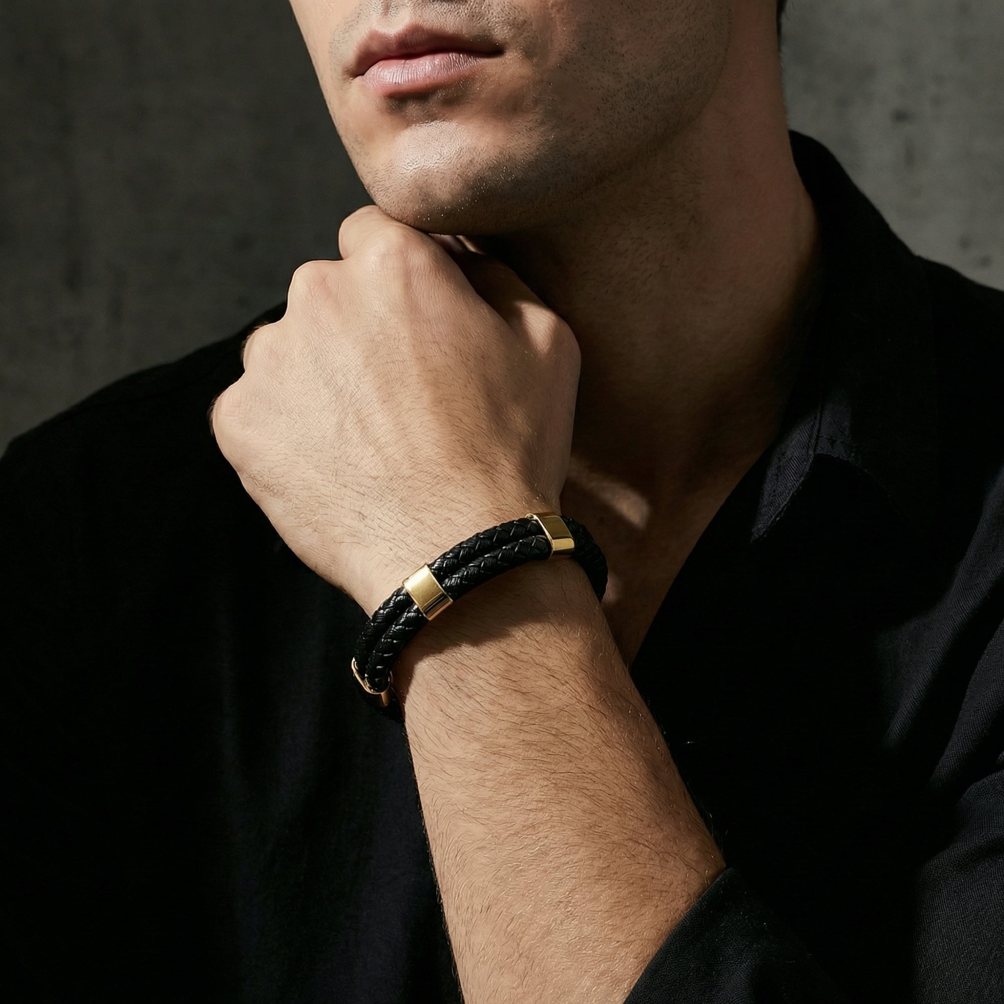 The Obsidian Braid Bracelet in black leather and gold stainless steel worn on a man's wrist.