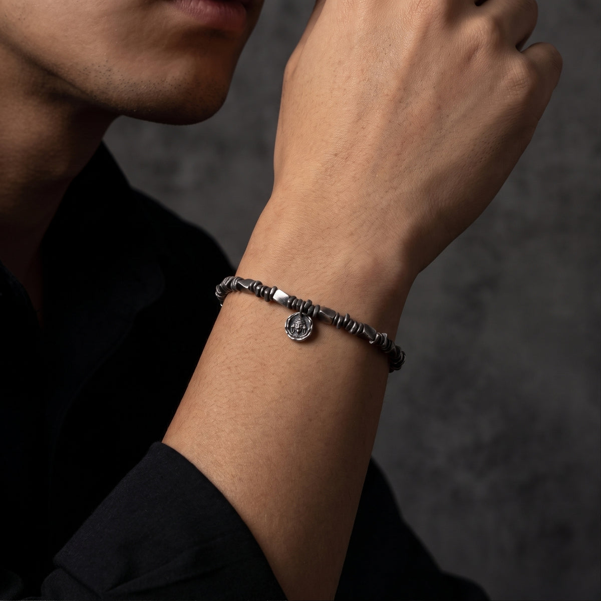 Close-up of the silver textured link bracelet with hanging medallion worn on a man's wrist.