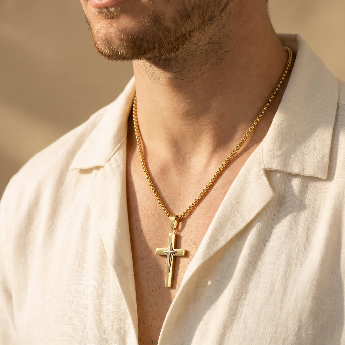 Close-up of a man wearing the gold-tone star cross pendant over an open cream shirt.