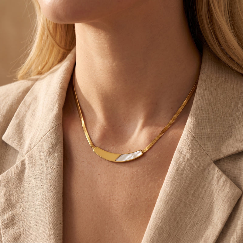 Gold flat snake chain necklace with mother of pearl accent worn by a model in a beige blazer.