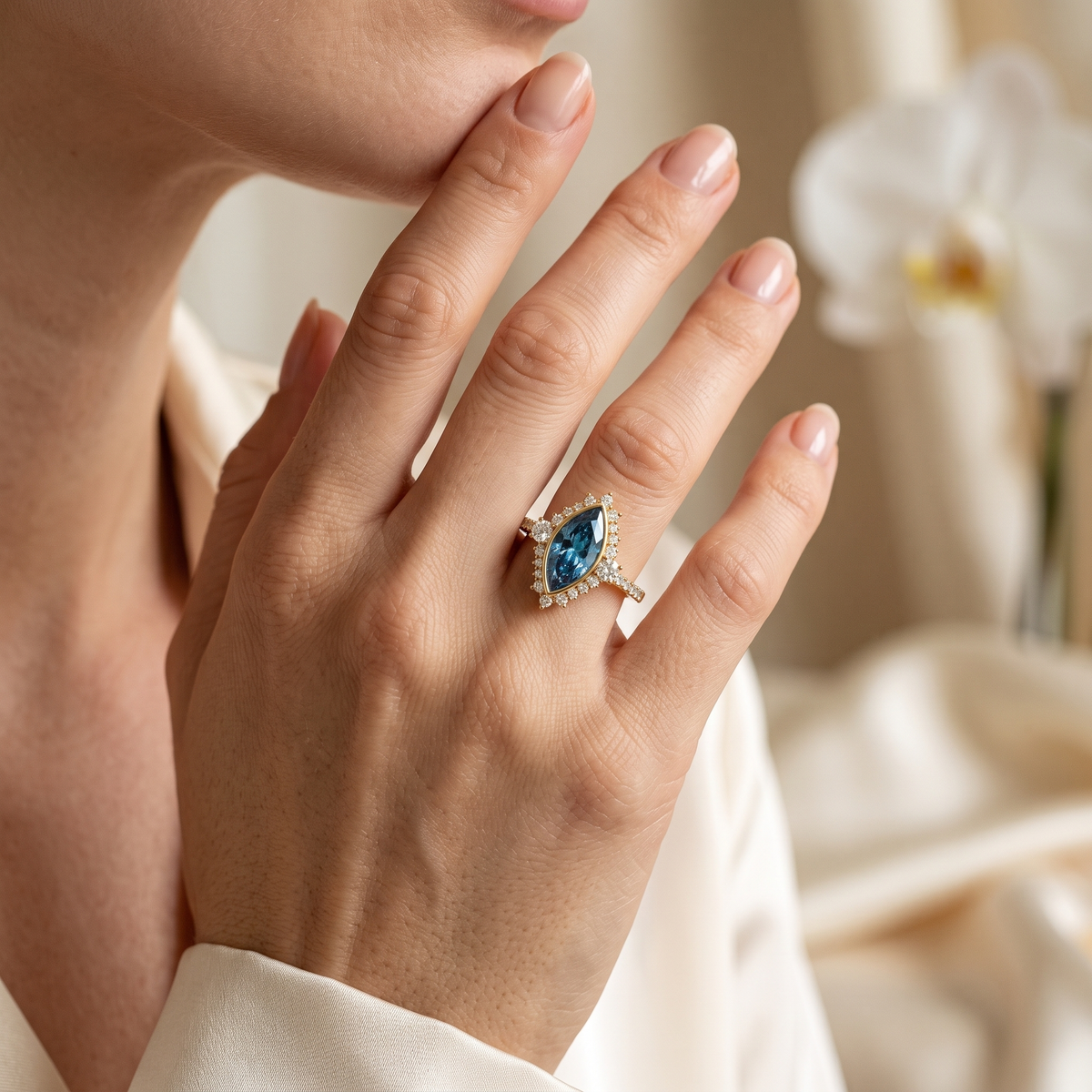Close-up of a marquise-cut blue gemstone halo ring in rose gold worn on a woman's finger.