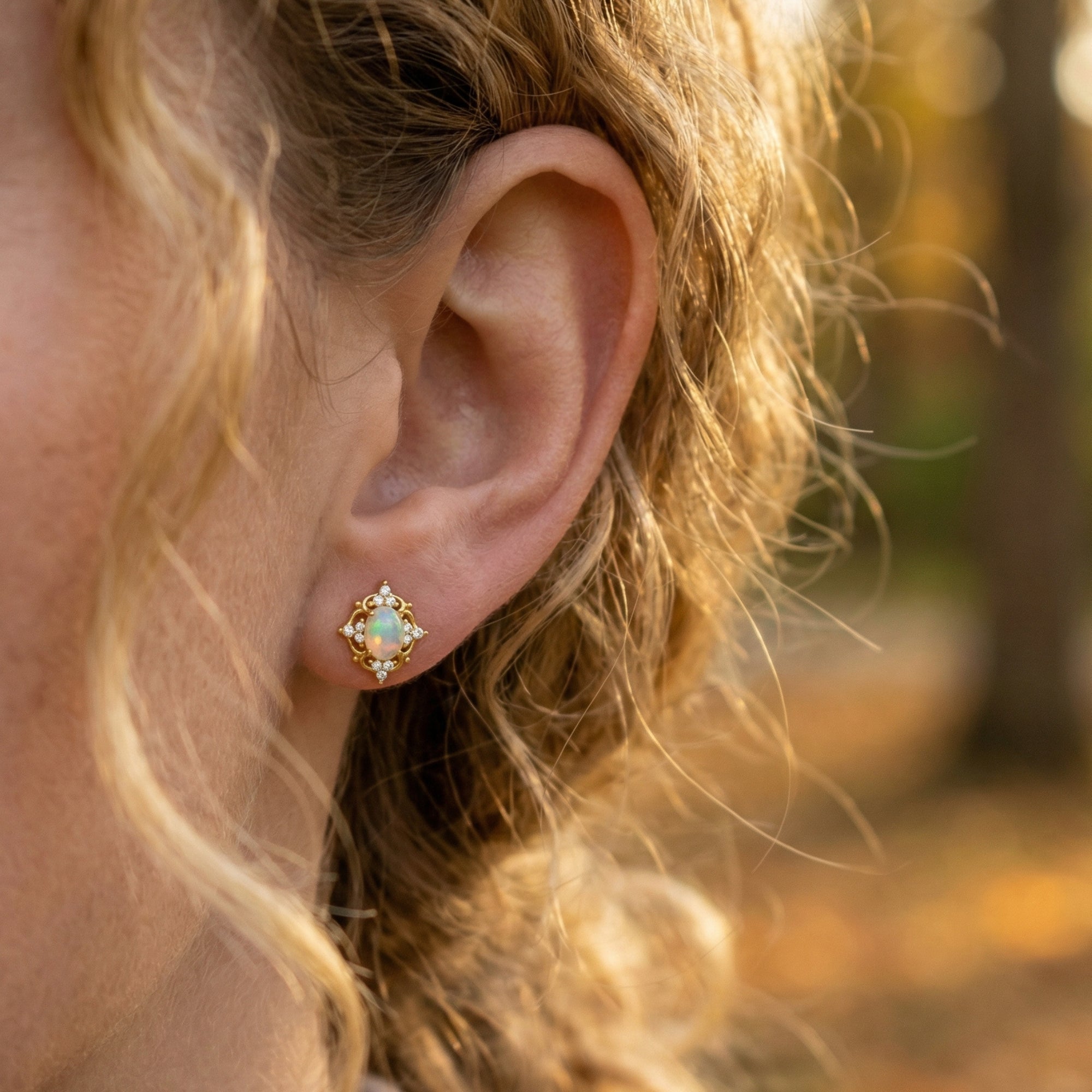 Model wearing a gold-tone sterling silver earring with an oval white opal and decorative filigree border.