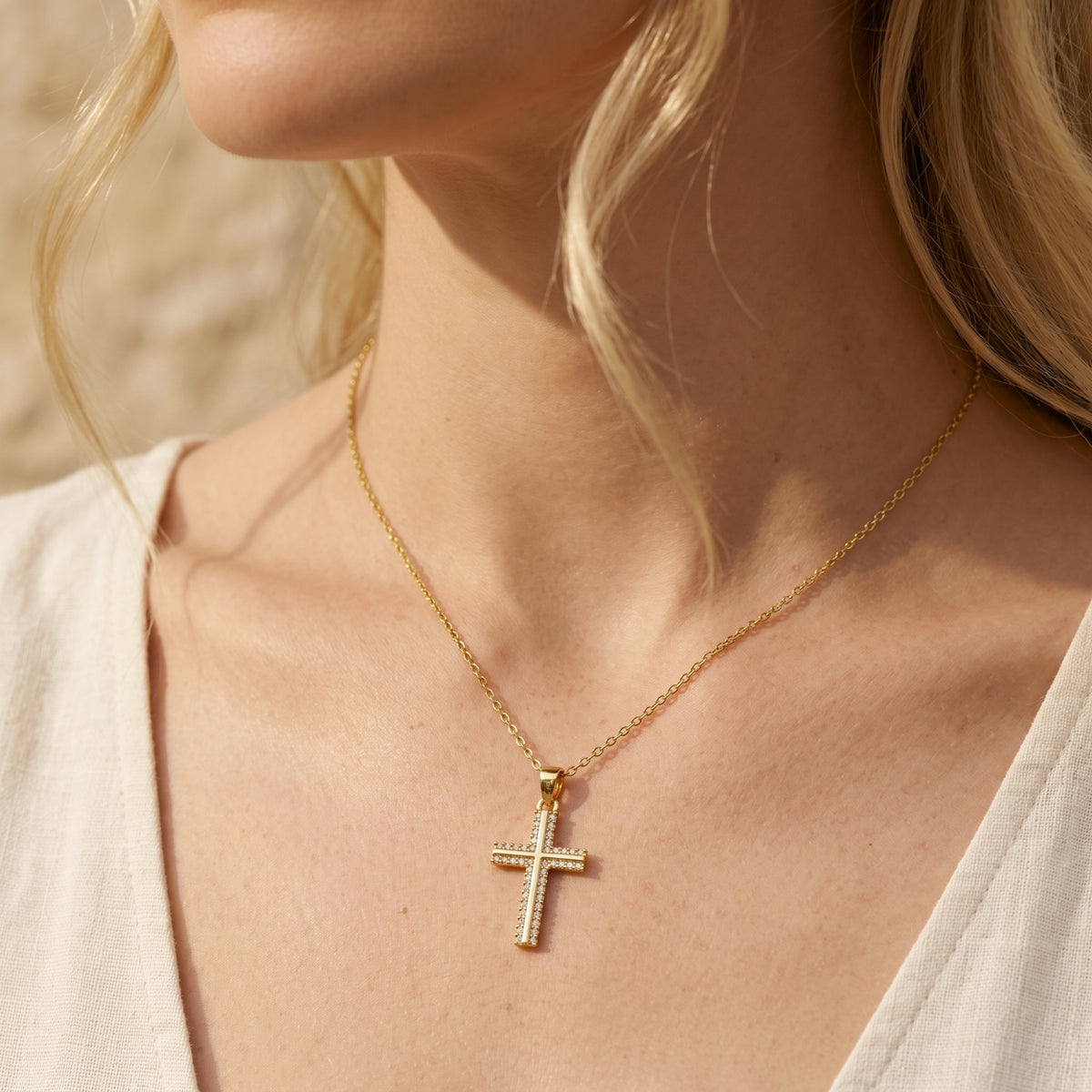 Gold-tone pavé cross necklace worn at the collarbone on a model.