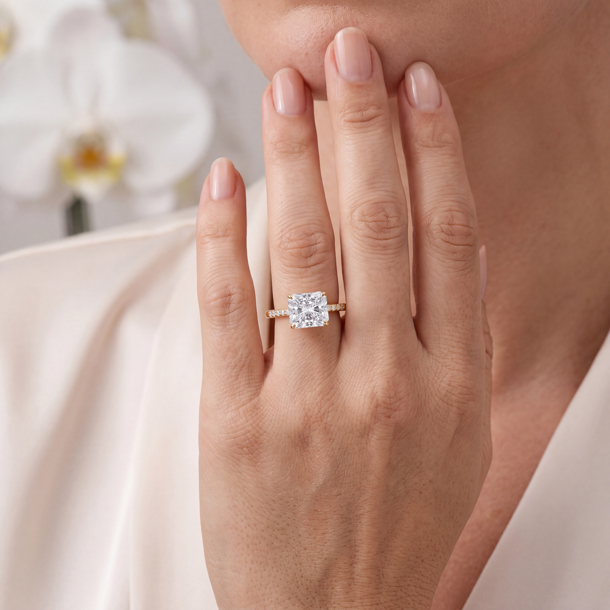 Yellow gold radiant cut moissanite engagement ring with a pavé band worn on a hand.