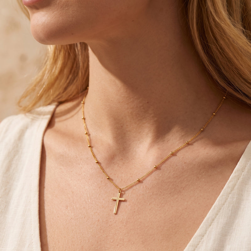 Close-up of a model wearing a gold-tone cross pendant on a beaded station chain.