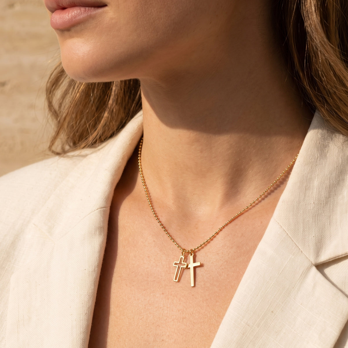 Close-up of a model wearing the gold-tone double cross necklace with solid and outline cross charms.