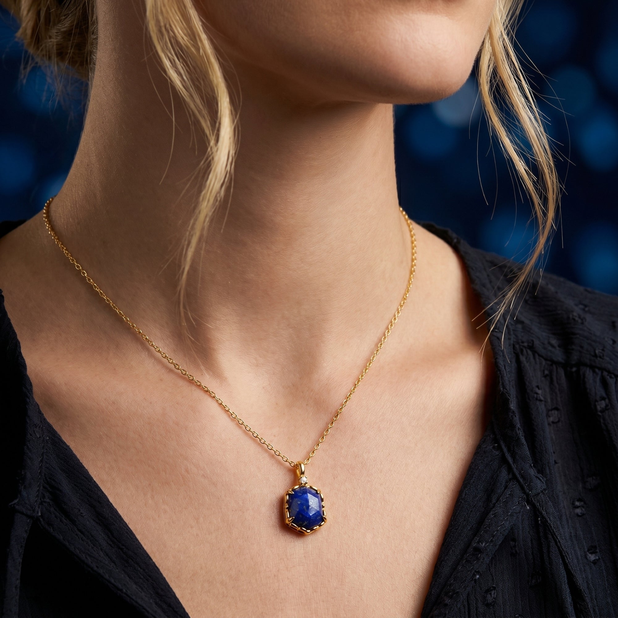 Gold plated hexagon lapis lazuli necklace worn by a model against a dark blue bokeh background.