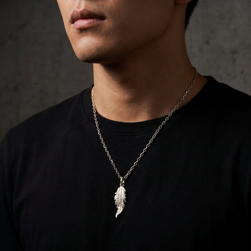 Man wearing the silver feather pendant necklace on a chain over a black T-shirt.
