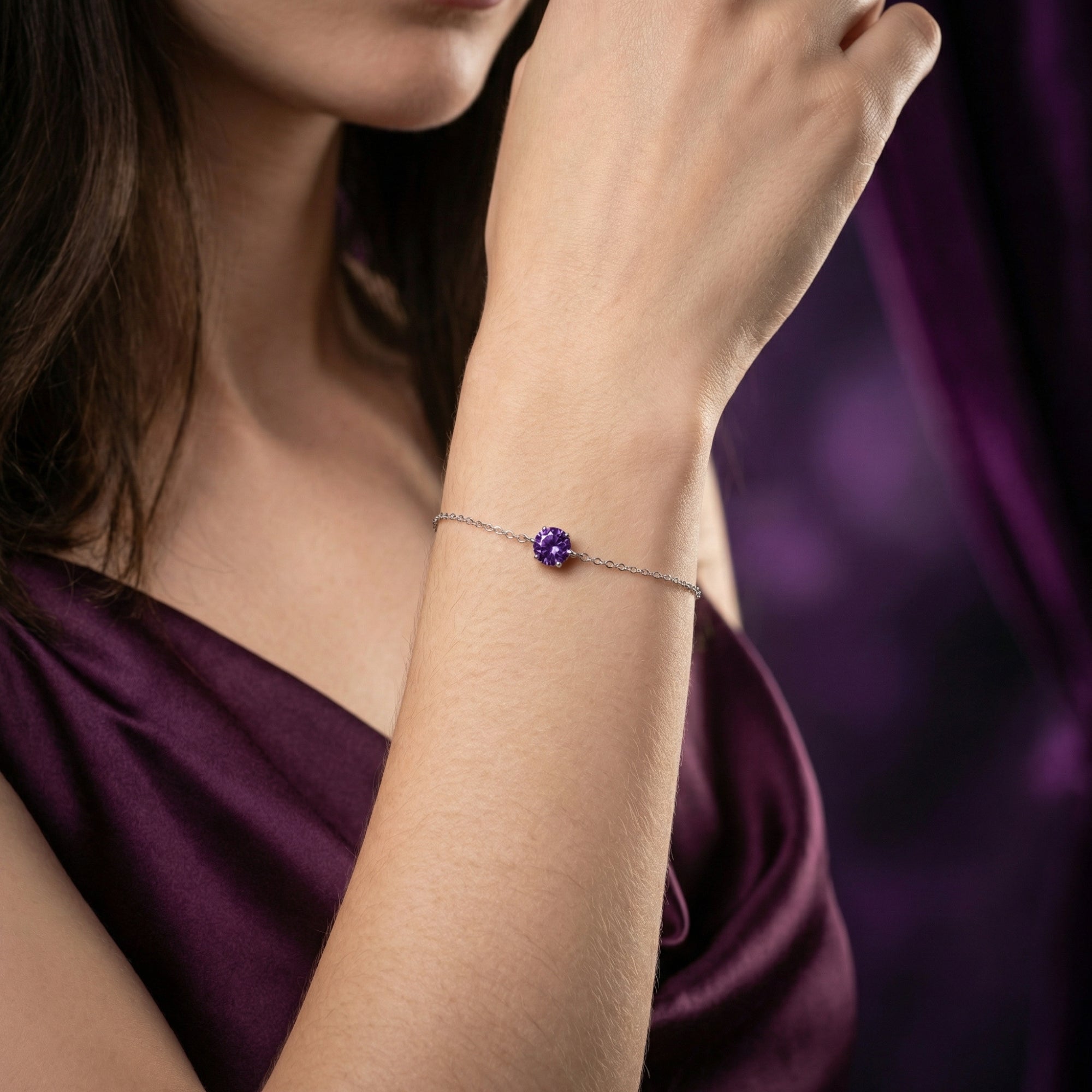 Round amethyst solitaire bracelet in sterling silver worn on a woman's wrist against a purple background.