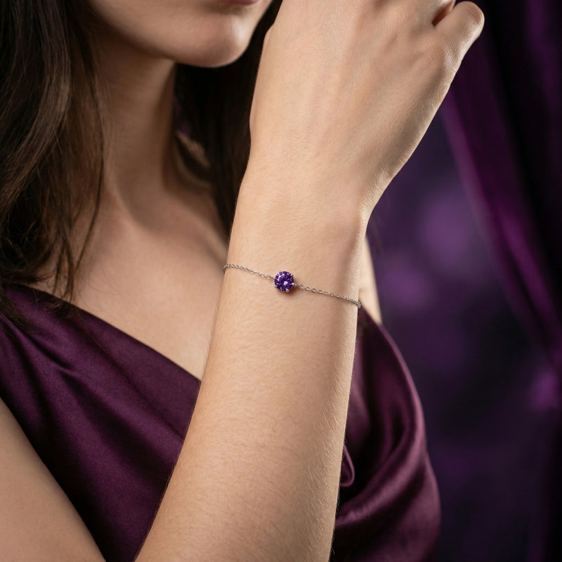 Round amethyst solitaire bracelet in sterling silver worn on a woman's wrist against a purple background.