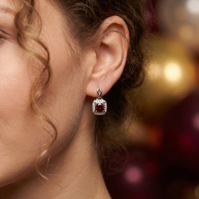 A woman wearing a round-cut garnet drop earring in sterling silver with a halo of zircon accents.